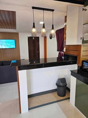 A modern kitchen with a black countertop, three pendant lights, a microwave, and a trash bin.