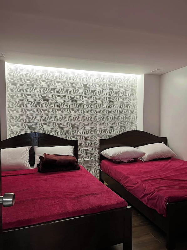 A room with two beds, each with a dark headboard and red bedding. The walls have a wavy pattern design.