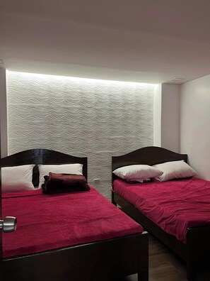 Une chambre avec deux lits, chacun doté d’une tête de lit sombre et d’une literie rouge. Les murs sont décorés d’un motif ondulé.
