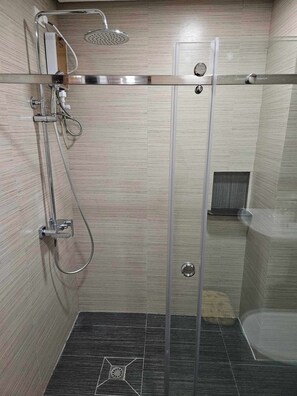 Une douche à l’italienne avec une porte en verre, une douchette à main et un robinet mural.