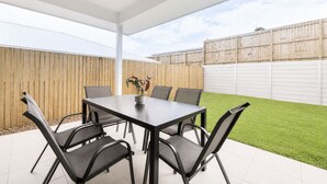 Un patio couvert avec une table et des chaises, une plante en pot et une clôture en bois en arrière-plan.