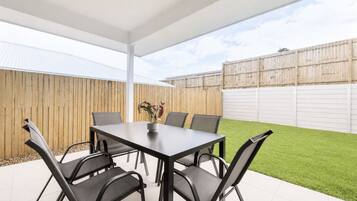 A covered patio area with a table and chairs, a potted plant, and a wooden fence in the background.