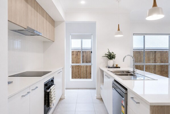 Cocina moderna con armarios blancos, horno empotrado, lavavajillas y ventana con vistas a madera.