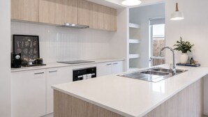 Une cuisine moderne avec des meubles blancs, un four encastré, un évier en acier inoxydable et des luminaires suspendus.