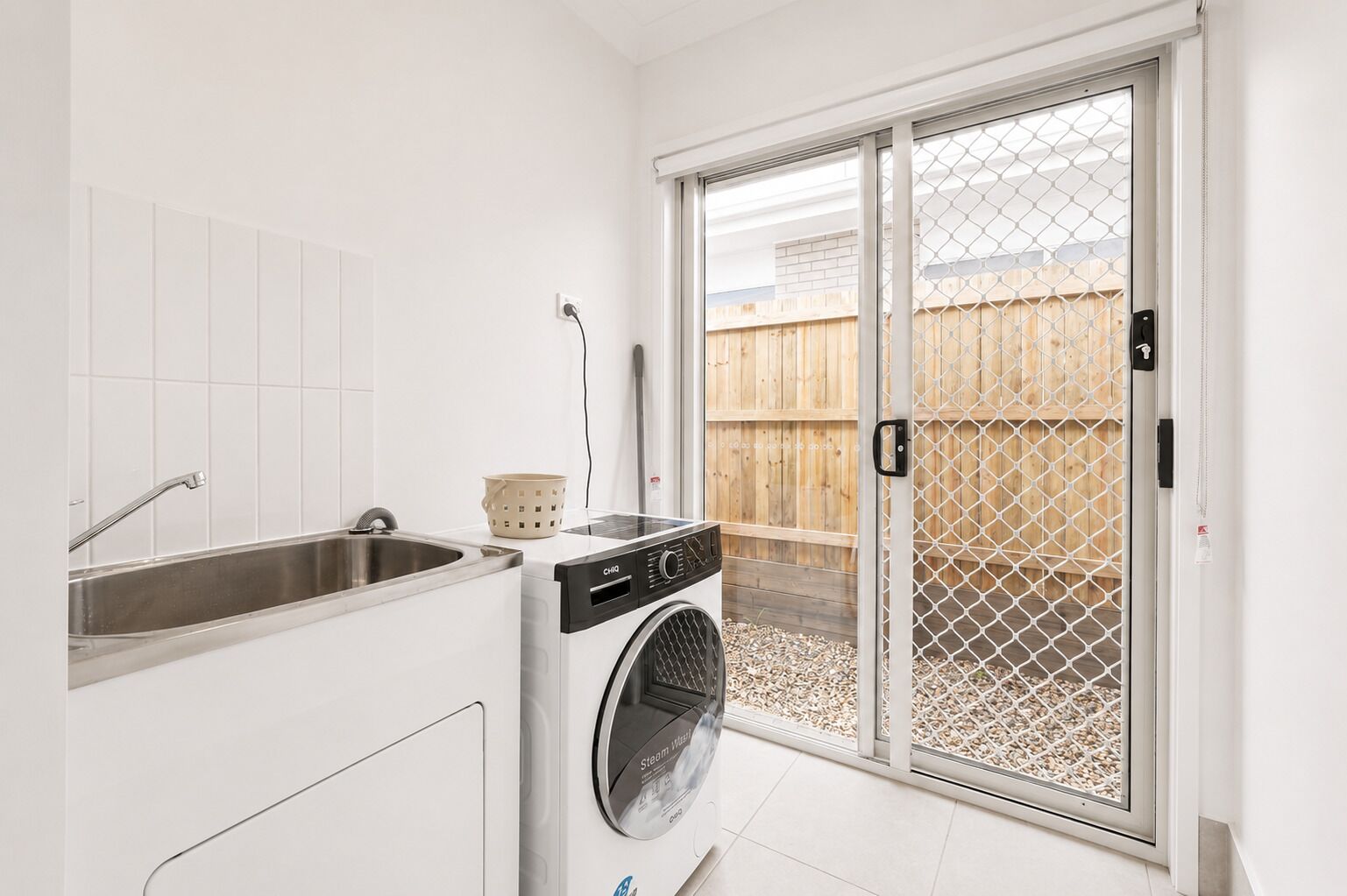 Cocina compacta con lavamanos integrado, lavadora y puerta corredera de vidrio que da a un patio trasero con cerca de madera.