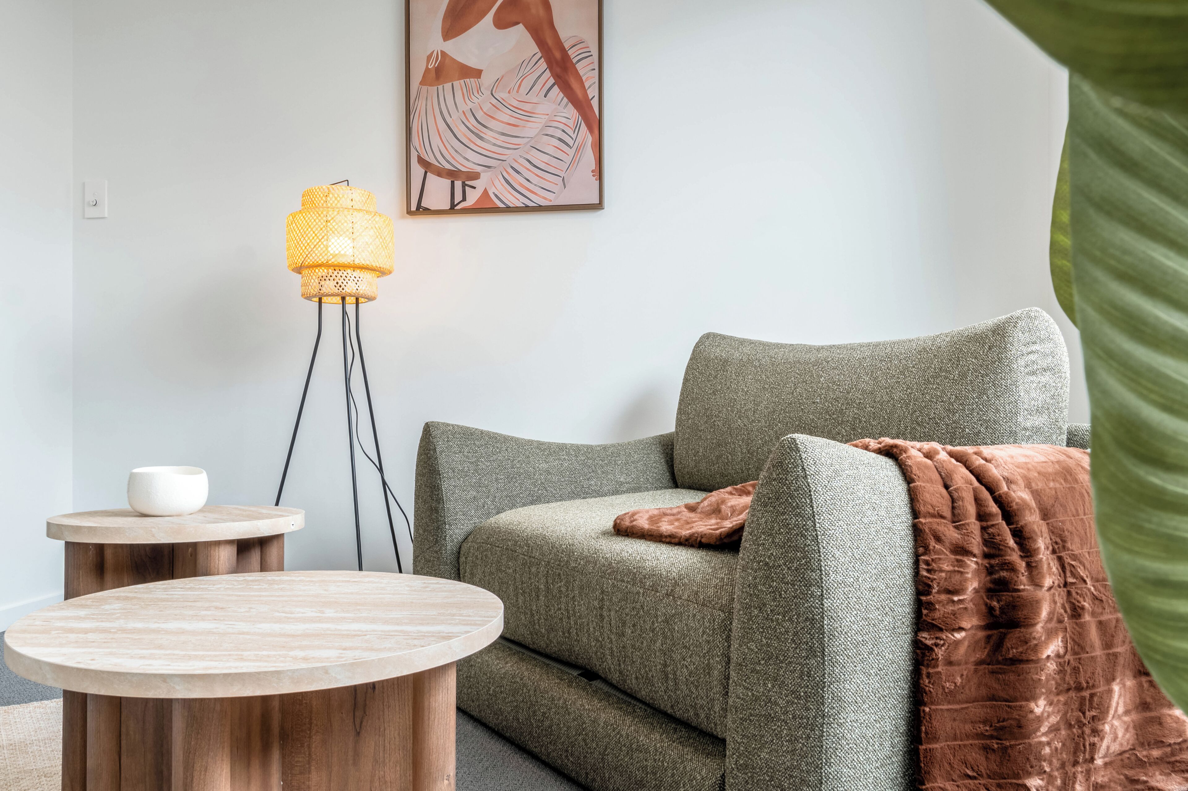 A living room with a green sofa, a round wooden table, a floor lamp, and a painting on the wall.