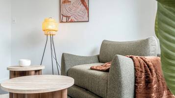 A living room with a green sofa, a round wooden table, a floor lamp, and a painting on the wall.