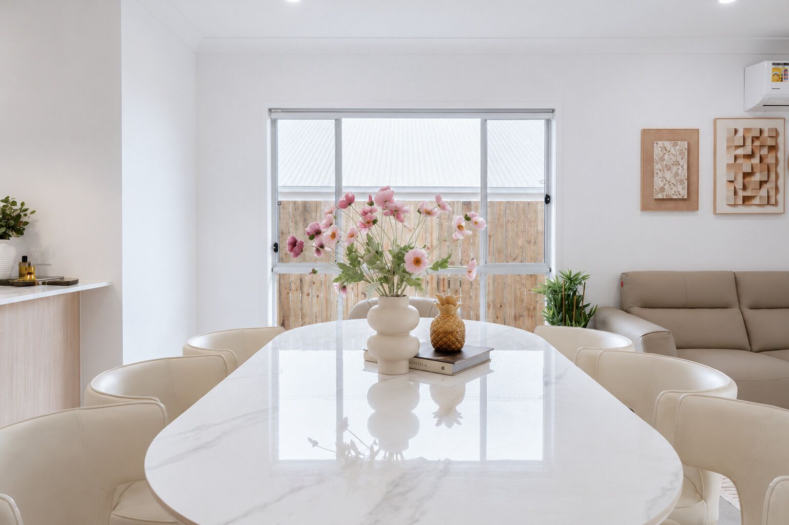 Un comedor moderno con una mesa de mármol, sillas blancas y un florero con flores.
