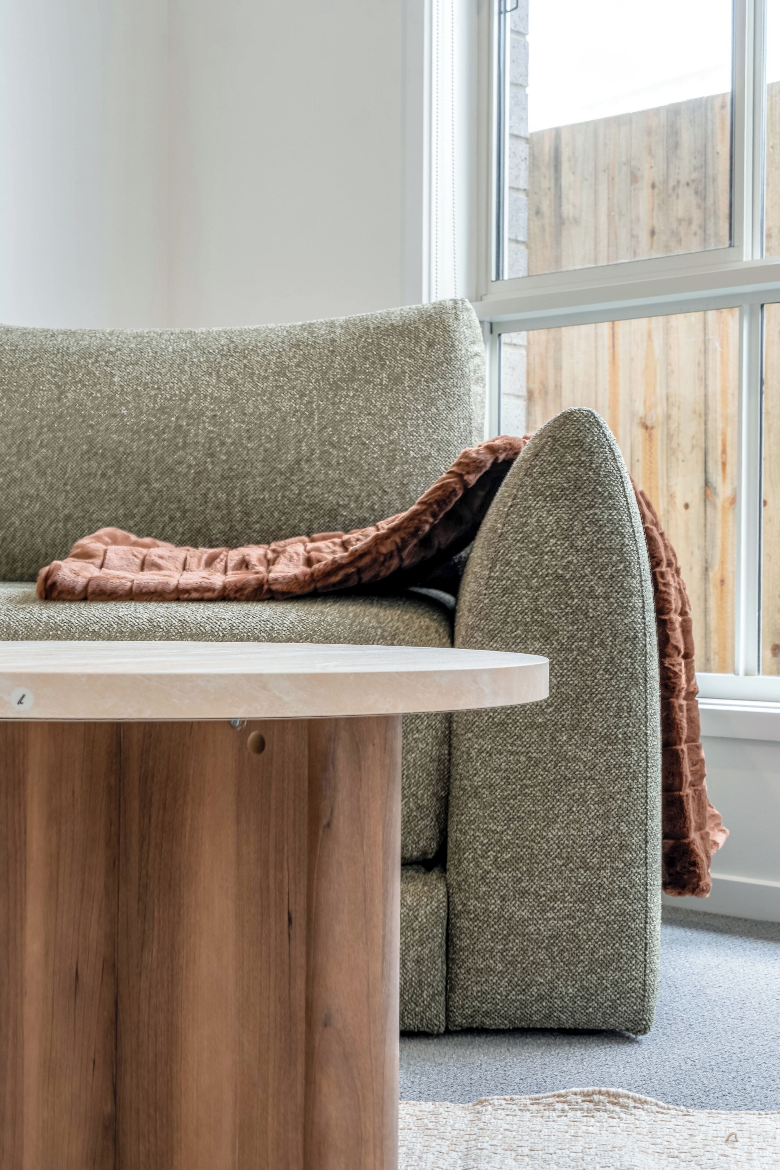 A room with a wooden coffee table, a green sofa, and a window with a view of a wooden fence.