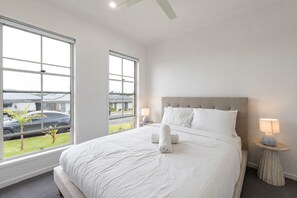 Habitación de hotel con una cama grande, dos lámparas de noche y vistas a un estacionamiento a través de las ventanas.