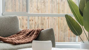 Une pièce avec un canapé gris, un plaid marron, un bol blanc posé sur une table ronde et une grande plante verte dans un pot blanc.