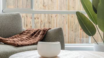A room with a grey sofa, a brown throw blanket, a white bowl on a round table, and a large green plant in a white pot.