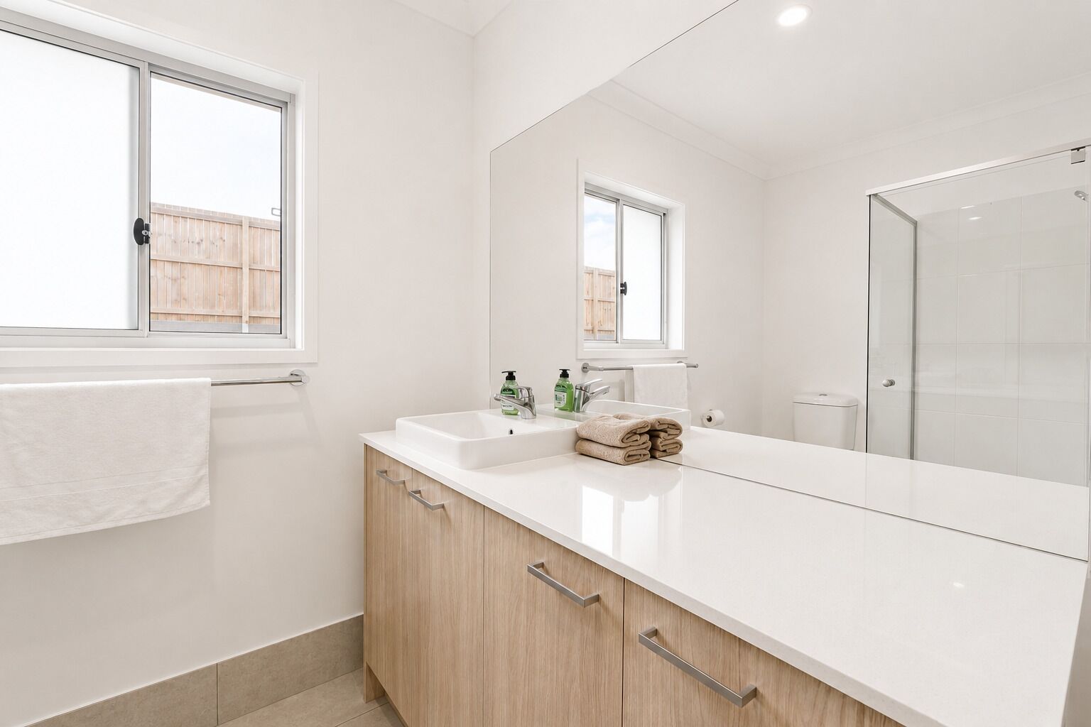 A modern bathroom with a large mirror, a white sink, and wooden cabinets.