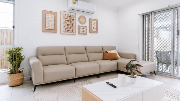 Un salon moderne avec un canapé d’angle beige, une table basse blanche et une plante en pot.