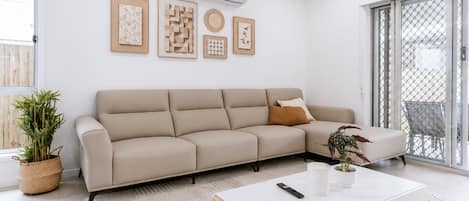 A modern living room with a beige sectional sofa, a white coffee table, and a potted plant.