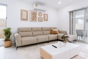 Una sala moderna con un sofá seccional color beige, una mesa de centro blanca y una planta en maceta.