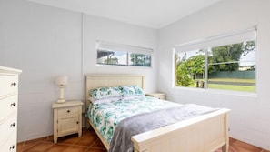 Un dormitorio con cama, mesitas de noche, cómoda y ventana con vista a follaje.