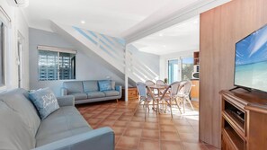 Una sala de estar moderna con un sofá, una mesa de comedor y sillas, una televisión y vistas al exterior.