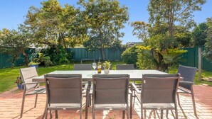 An outdoor patio with a table and chairs, surrounded by greenery and a fence.