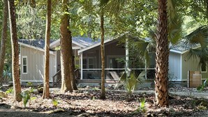 Ein Haus mit Veranda, umgeben von Bäumen und einer Schotterauffahrt.