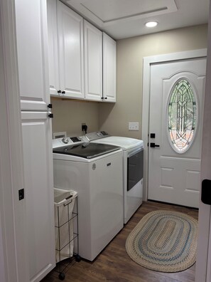 A compact kitchen with white cabinetry, a built-in washer and dryer, and a door with a stained glass window.