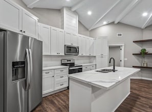 A modern kitchen with white cabinetry, stainless steel appliances, and a marble countertop island.