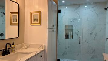 A modern bathroom with a glass-enclosed shower, marble tiles, a sink with a black faucet, and framed pictures on the wall.