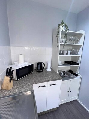A compact kitchen with a microwave, kettle, and a shelf with glasses and cups. - u2-Cute Fresh Unit|Quiet Centre|NewAC|SmartTV (Norman Park)