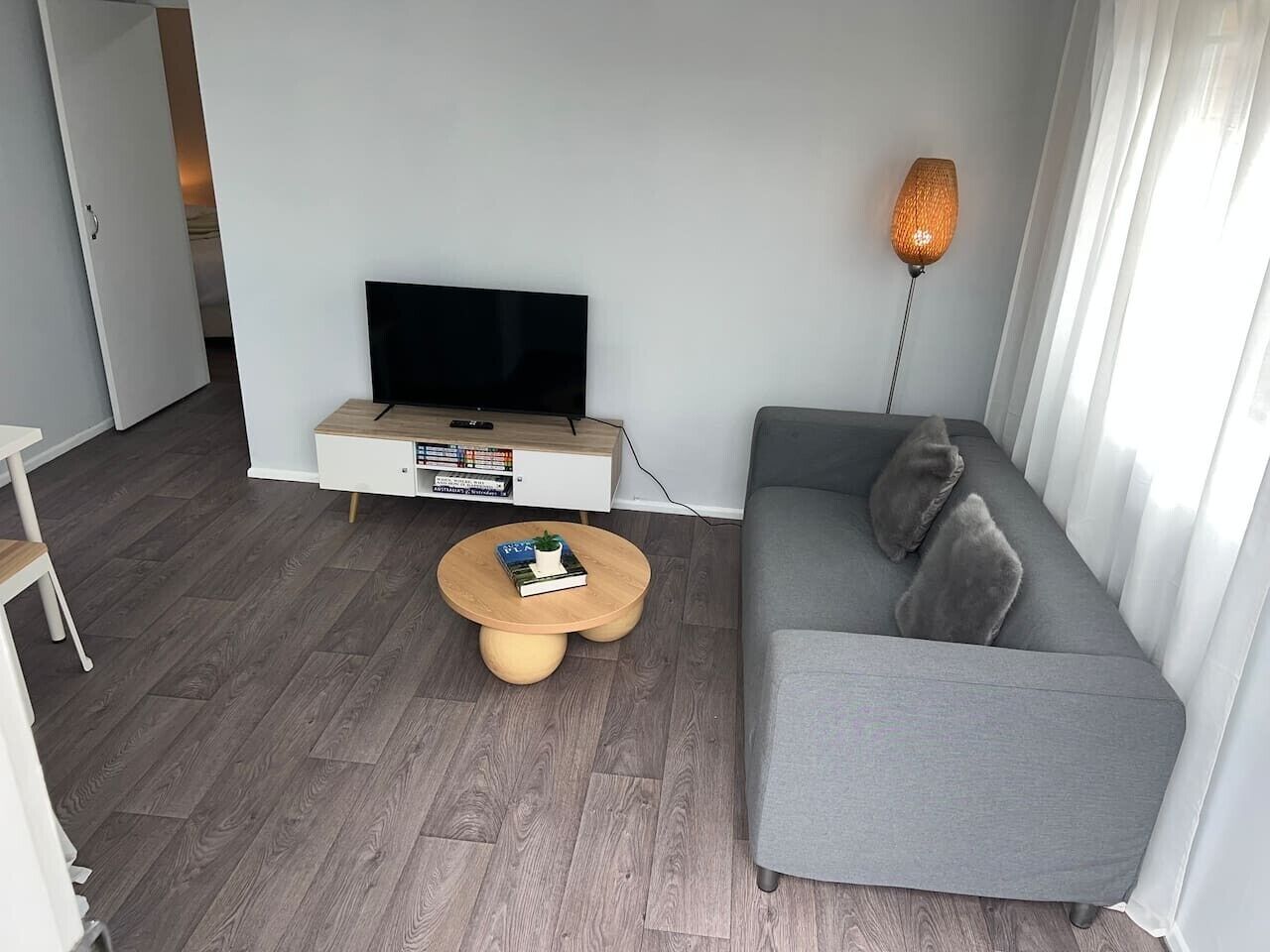 Un soggiorno moderno con un divano grigio, un tavolino rotondo in legno, un televisore a schermo piatto su un mobile bianco e una lampada da terra.