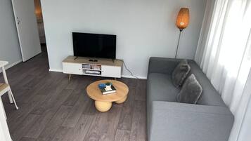 Un soggiorno moderno con un divano grigio, un tavolino rotondo in legno, un televisore a schermo piatto su un mobile bianco e una lampada da terra.