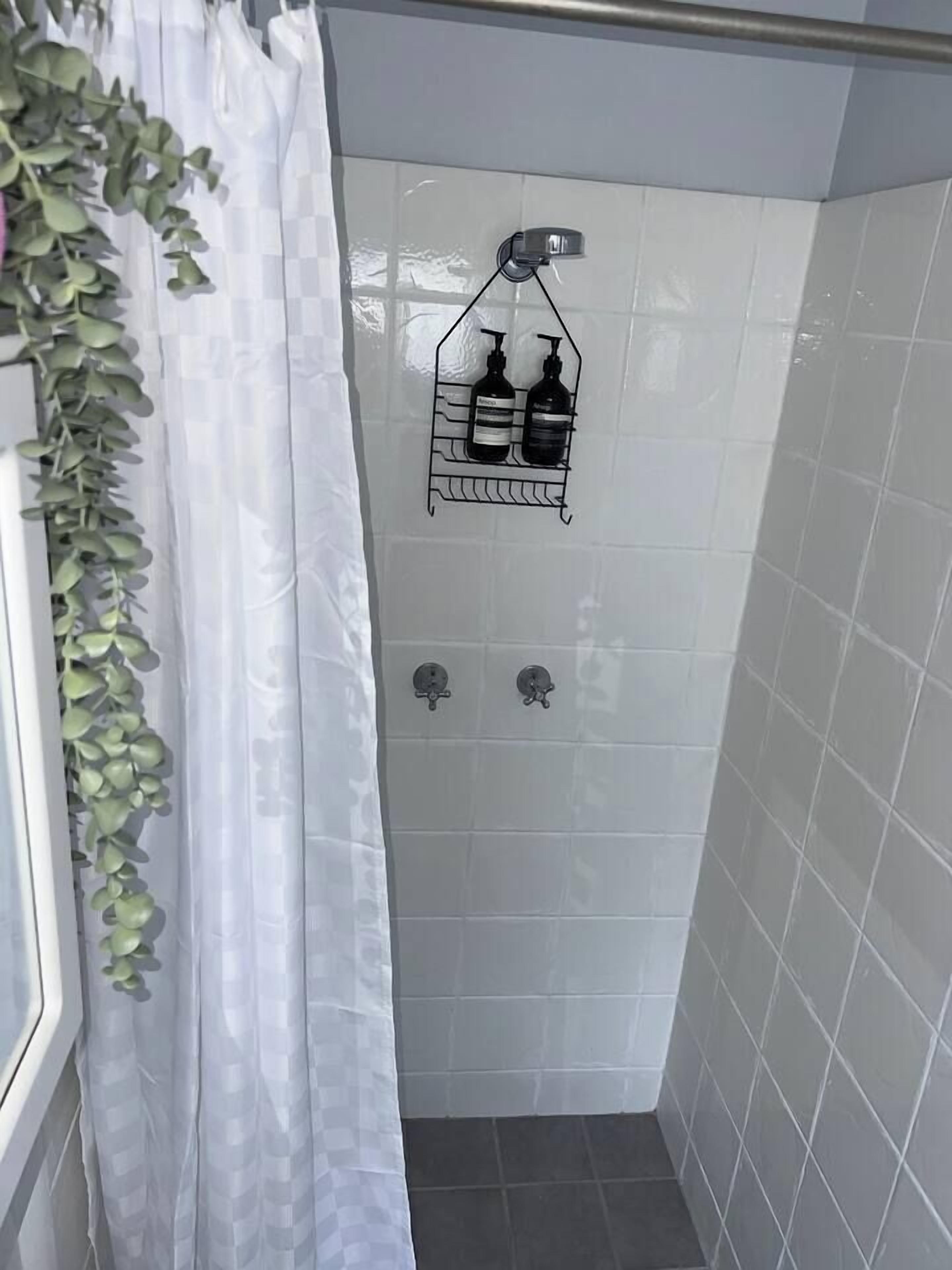 Área de duche com parede revestida a azulejos brancos, cortina de chuveiro e suporte de metal para artigos de higiene.