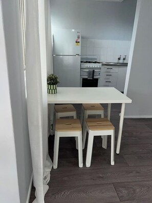 A compact kitchen with a white countertop, a gas stove, and a refrigerator. There are four wooden stools under the counter. - u2-Cute Fresh Unit|Quiet Centre|NewAC|SmartTV (Norman Park)