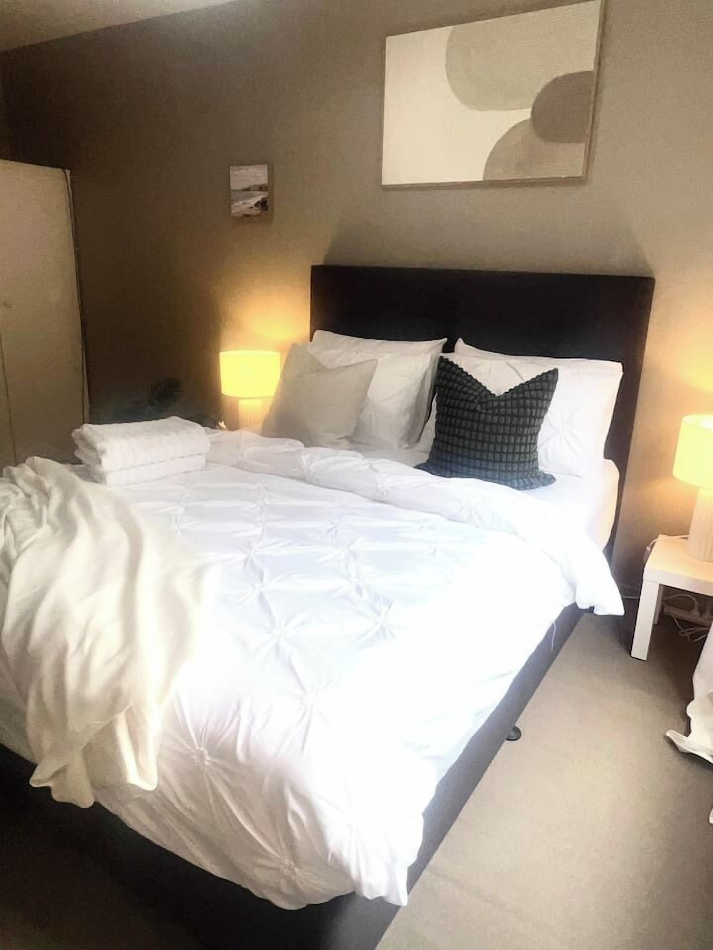 A hotel room with a bed, two bedside lamps, a headboard, and a wall-mounted artwork.