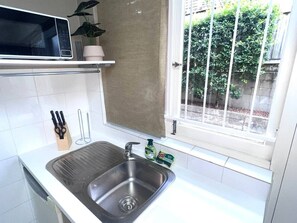 Cocina con pileta de acero inoxidable, microondas y ventana con vista a follaje exterior.