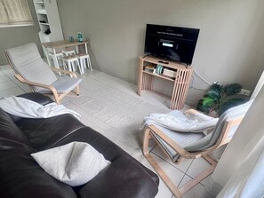 A living room with a sofa, two chairs, a TV on a wooden stand, and a small table with drinks.