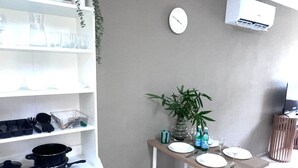 Et køkken med en hvid bordplade, et spisebord med stole, et ur og en aircondition på væggen.