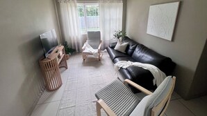 A living room with a television, a sofa, a chair, and a table. - u4-Traditional Unit-Quiet Close CBD-AirConSmartTV (Norman Park)