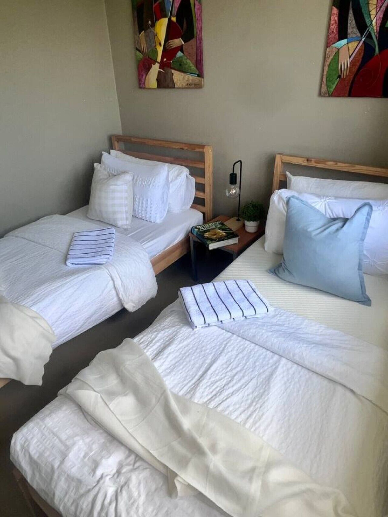 Una camera d'albergo con due letti, ciascuno con biancheria e cuscini bianchi. C'è un comodino con una lampada e un libro.