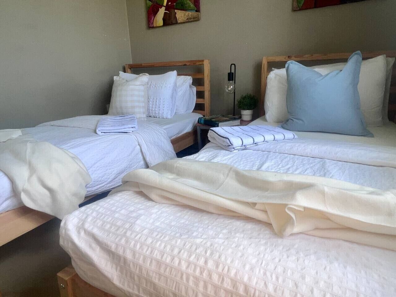 Ein Hotelzimmer mit zwei Betten, jeweils mit weißer Bettwäsche und Kissen, einem Nachttisch mit Lampe und einer kleinen Topfpflanze.