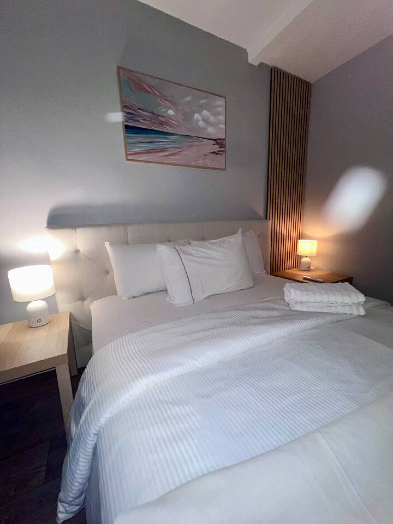 Ein Hotelzimmer mit einem großen Bett, zwei Nachttischlampen, einem Bild an der Wand und einer Holzwand rechts.