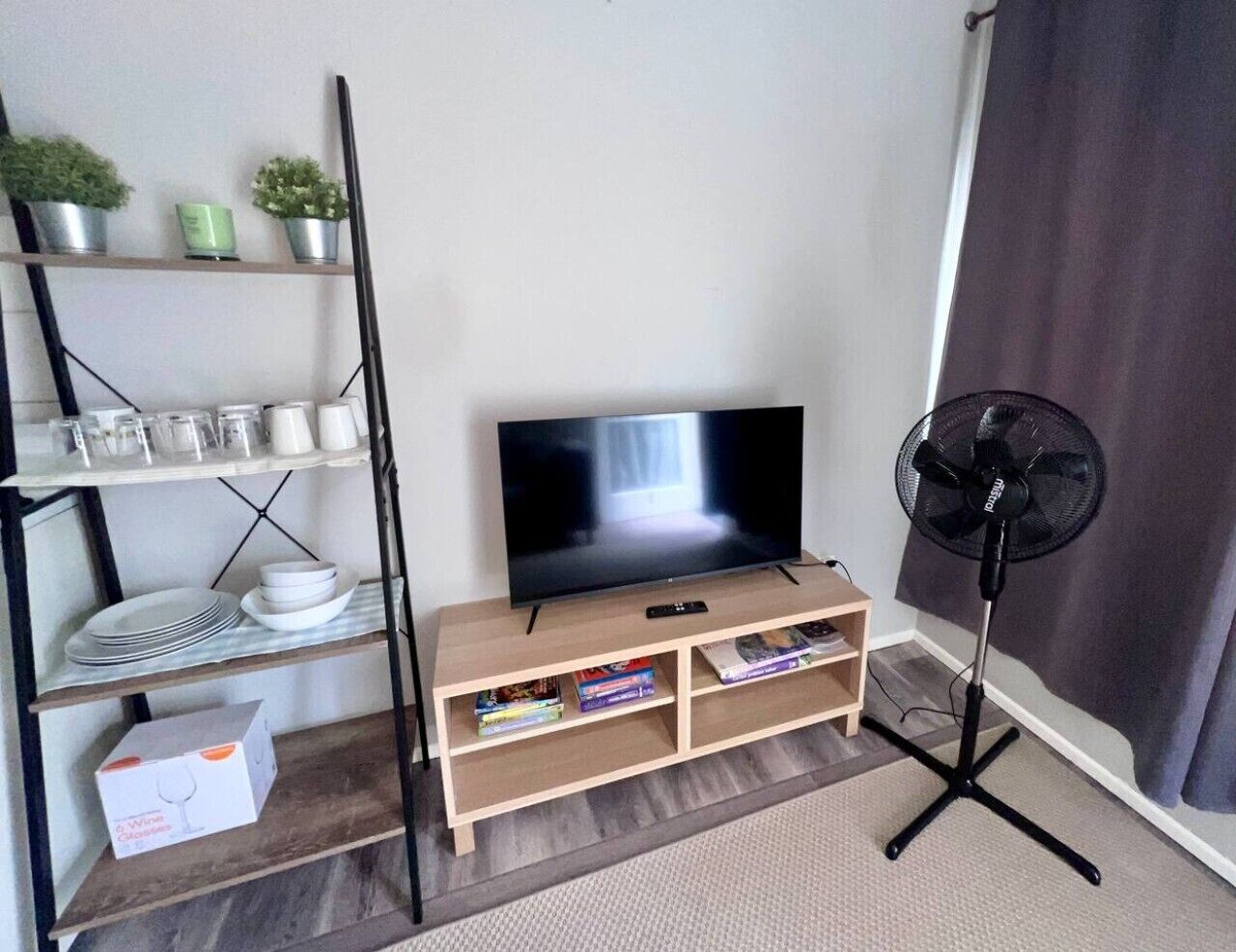 Ein Wohnzimmer mit Fernseher, Ventilator und Regalen mit Gegenständen.