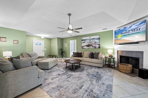 A living room with a ceiling fan, a fireplace, and a television displaying 'Gold Star Vacation Rentals'. - Coastal Orange Beach Retreat | Minutes to the Beach, The Wharf & Family Fun (Orange Beach)