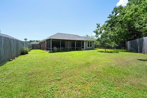 A residential backyard with a covered patio, a wooden fence, and a tree. - Coastal Orange Beach Retreat | Minutes to the Beach, The Wharf & Family Fun (Orange Beach)