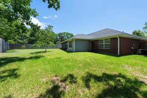 A single-story house with a covered garage, a fenced yard, and a tree. - Coastal Orange Beach Retreat | Minutes to the Beach, The Wharf & Family Fun (Orange Beach)