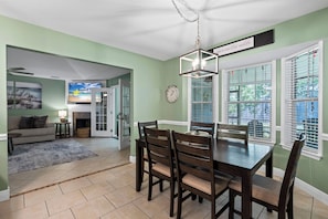 A dining area with a wooden table and chairs, a clock on the wall, and a view of the outdoors through the windows. - Coastal Orange Beach Retreat | Minutes to the Beach, The Wharf & Family Fun (Orange Beach)