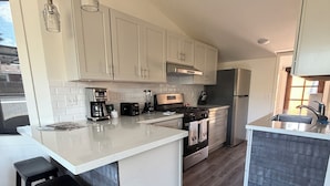 A modern kitchen with white cabinetry, a central island with stools, a built-in oven, and a stainless steel refrigerator.