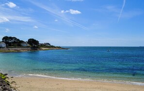 Ein Strand mit klarem Wasser, einem Sandufer und einer Reihe von Häusern im Hintergrund.