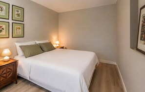 Ein ordentlich bezogenes Bett mit weißen Leinentüchern und zwei Kissen, an beiden Seiten zwei Nachttische mit Lampen, in einem Raum mit hellen Wänden und Holzdielen.