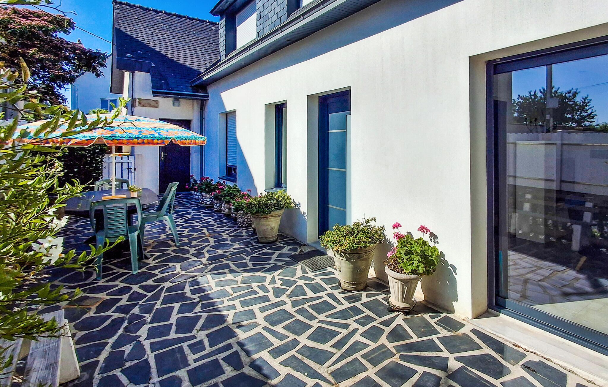 A courtyard with a tiled floor, potted plants, a table with chairs, and a large umbrella.