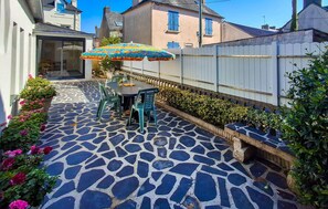 Eine Terrasse mit einem gemusterten Steinboden, einem Tisch mit Stühlen und einem farbenfrohen Sonnenschirm.